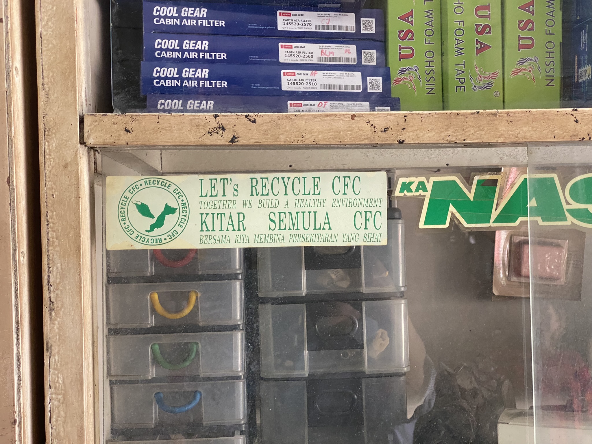A sticker on a cabinet in a Malaysian air conditioner repair shop. In the 1990s, the government funded training for technicians on the environmental impacts of CFC-12 emissions from motor vehicles. But similar trainings haven't been continued for gases such as HFC-134a. Photo: Tilden Chao, 2023.