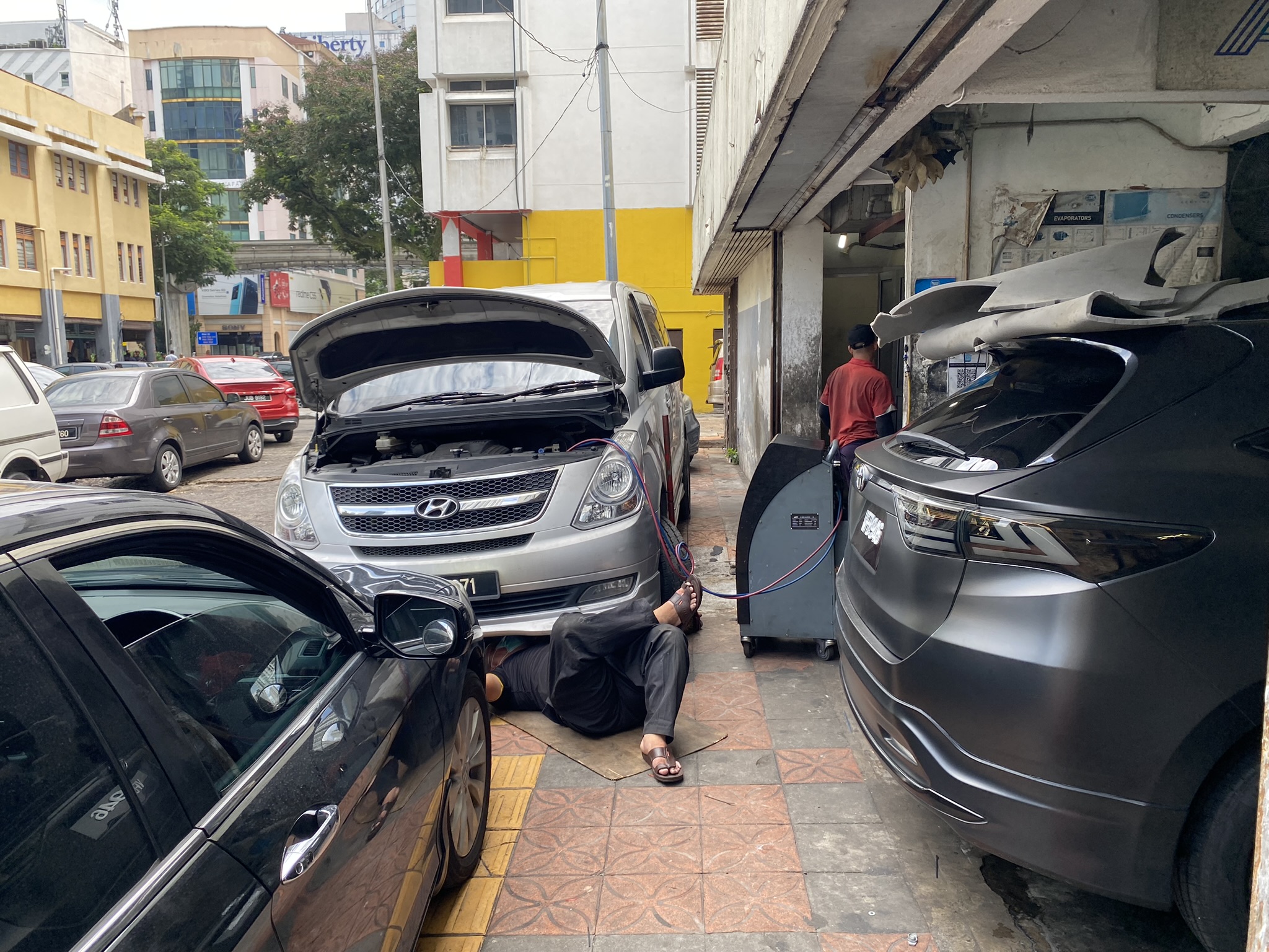 A mechanic repairing a car air conditioner at Ming Wah Car Cooler in Kuala Lumpur. Next to him is a refrigerant recovery machine, which helps mechanics cut costs and prevent emissions during servicing. Photo: Tilden Chao, 2023.